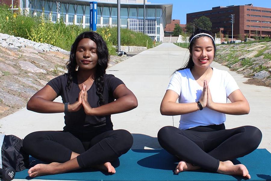 2 students do yoga campus center lawn.