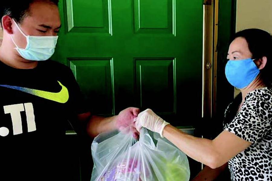 Two asian people wearing masks hold plastic bags of food at a doorway.